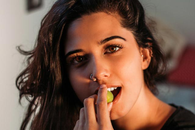 mulher com piercing comendo uma uva