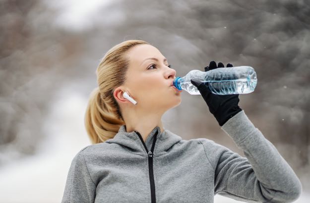 Desportista fazendo uma pausa e bebendo água em pé na natureza em um dia de inverno. 