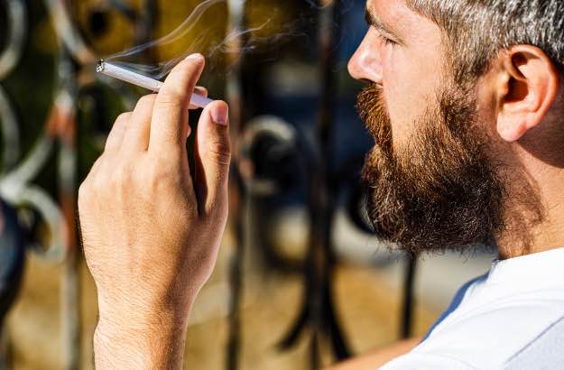 Homem com barba fumando cigarro. 