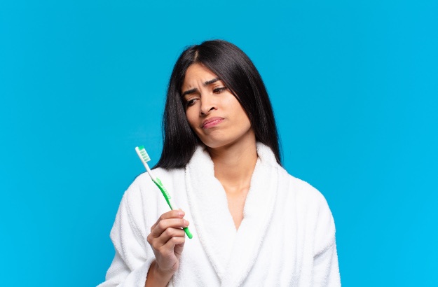 Jovem mulher, hispanica com uma escova de dentes, com fundo azul. 