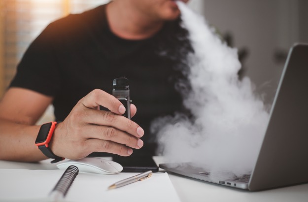 Jovem usando cigarro eletrônico descartável na mesa do escritório