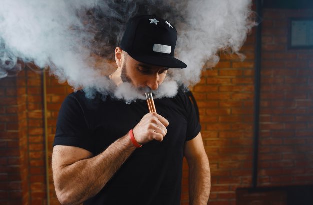 Homem de boné e camiseta preta usando vape 