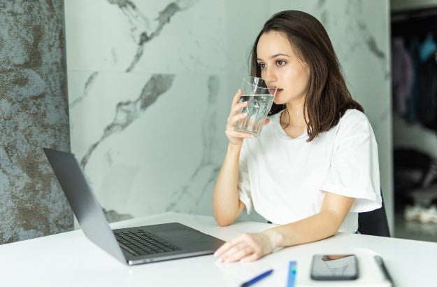 Jovem moça bebendo água em escritório 