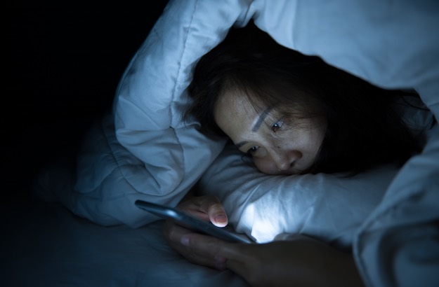 Mulher asiática com hábitos noturnos, dormindo tarde por ficar usando smartphone