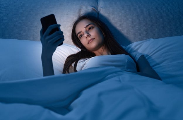 Jovem mulher dormindo tarde por ficar no celular até altas horas da noite