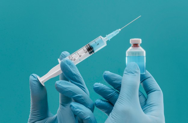 Médico com luvas azul segurando seringa com agulha e um frasco de vacina 