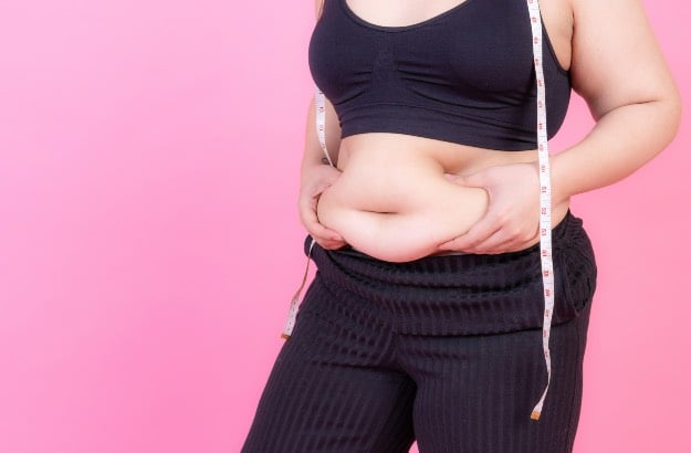 Mulher com sobrepeso aperta a gordura na barriga com fita métrica