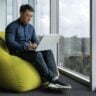 Asiático jovem trabalhador de escritório sentado em pulfe macio programador usando laptop escrevendo código