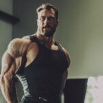 Chris Bumstead fazendo pose na sala de pose na academia para treinar a performance no palco