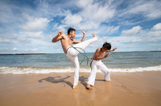 Dois jovens praticando capoeira na praia 