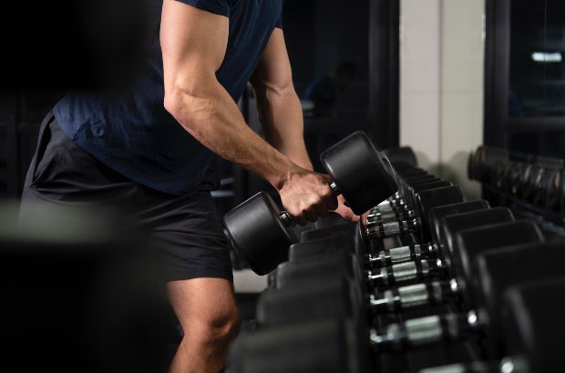 Homem com porte atlético na academia peganto halter para realizar treino ABC 