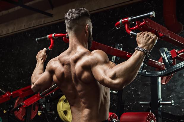 Homem porte atlético treinando em academia para buscar definição muscular 