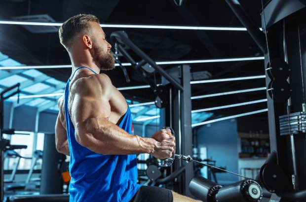 Homem porte atlético treinando em academia para definição muscular 