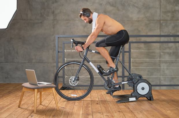 Homem treinando HIIT na bike para definição muscular vendo a importância da intensidade do exercício no computador 
