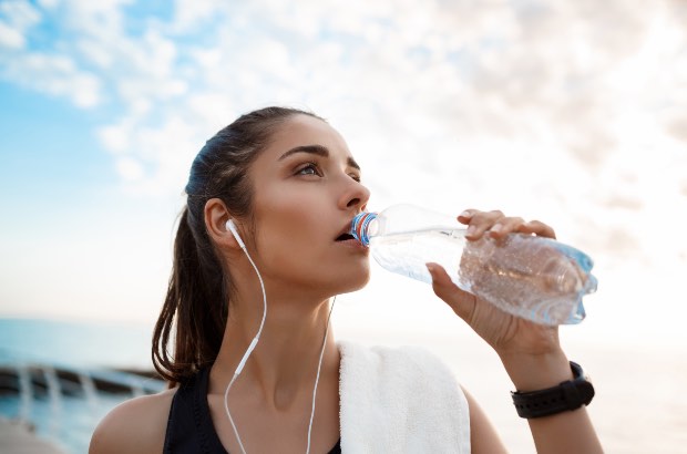 Menina praticando esporte com fones de ouvido da uma pausa para se hidratar 