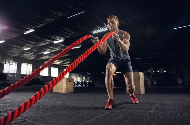 Jovem saudável atleta fazendo exercício com cordas na academia, treino nível hard