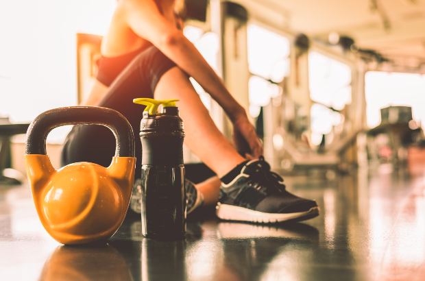 Mulher descansando ao lado de kettlebell e garrada de água na academia 