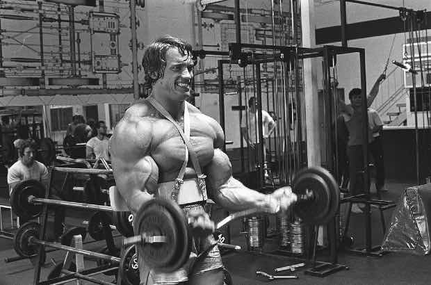 Arnold Schwarzenegger treinando bíceps para competição de fisiculturista 