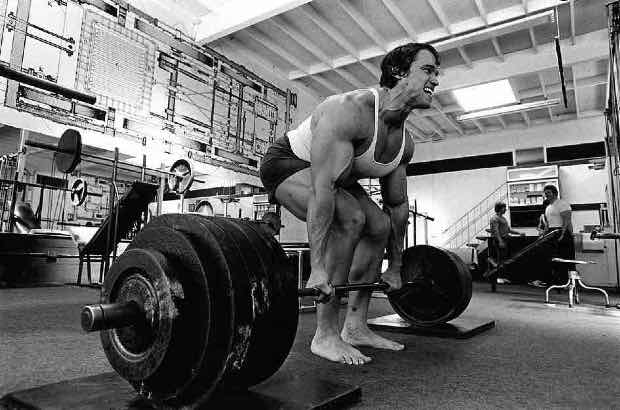 Arnold Schwarzenegger treinando levantamento de peso em academia  para competição de fisiculturismo 