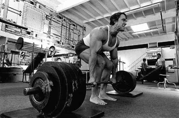 Arnold Schwarzenegger treinando levantamento de peso em academia  para competição de fisiculturismo 